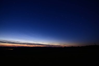 Büyük Ayı takımyıldızı, kuyruklu yıldız Lemmon ve yıldız bağlantı uydularıyla dolu renkli bir ufukta gün batımı..