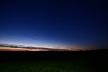 Büyük Ayı takımyıldızı, kuyruklu yıldız Lemmon ve yıldız bağlantı uydularıyla dolu renkli bir ufukta gün batımı..