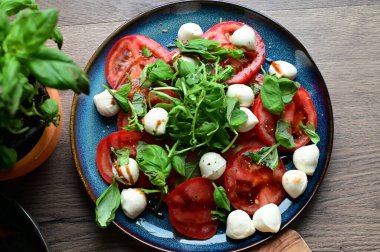 Bebek mozarella, olgun domatesler ve bitkilerle taze Caprese salatasının en iyi görüntüsü. Renkli ve canlı sunum, geleneksel İtalyan mutfağının içeriğinin tazeliğini ve basitliğini vurguluyor..