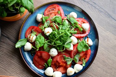 Bebek mozarella, olgun domatesler ve bitkilerle taze Caprese salatasının en iyi görüntüsü. Renkli ve canlı sunum, geleneksel İtalyan mutfağının içeriğinin tazeliğini ve basitliğini vurguluyor..