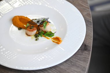 Deniz tarağı (St. Jacques), taze otlar ve ahşap bir masa üzerindeki bir restoranda zarif bir şekilde kaplanmış balkabağı içeren renkli aperatifler. Gurme, güzel yemekler ve aşçılık projeleri için mükemmel..