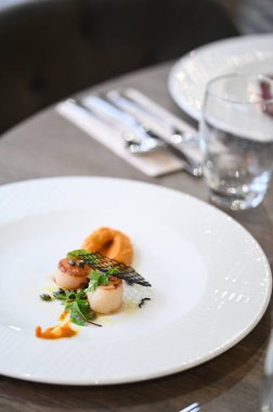 Deniz tarağı (St. Jacques), taze otlar ve ahşap bir masa üzerindeki bir restoranda zarif bir şekilde kaplanmış balkabağı içeren renkli aperatifler. Gurme, güzel yemekler ve aşçılık projeleri için mükemmel..