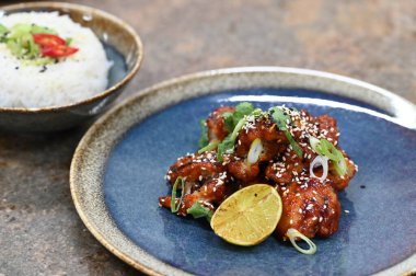 Susam tohumlu kızarmış tavuk ve taze limon dilimleri. Mavi tabakta pilavla servis ediliyor. Renkli ve iştah açıcı yemek sunumu, mutfak, restoran ve yemek temalı projeler için mükemmel.