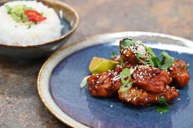Susam tohumlu kızarmış tavuk ve taze limon dilimleri. Mavi tabakta pilavla servis ediliyor. Renkli ve iştah açıcı yemek sunumu, mutfak, restoran ve yemek temalı projeler için mükemmel.