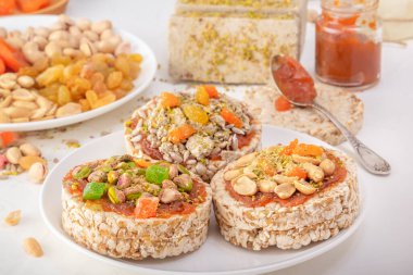 Fıstıklı patlamış buğday taneleri ve kurutulmuş kayısılar, şam fıstıkları ve ayçekirdeği, halva ve kuru üzümler beyaz bir tabakta kayısı reçeli ve doğu tatlılarının arka planında.