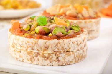 İnce bir tabaka kayısı reçeli üzerinde patlamış buğday taneleri ve şekerli meyveler ve patlamış buğday taneleri ve beyaz bir tabakta fıstık ve kurutulmuş kayısı. Yakın plan.