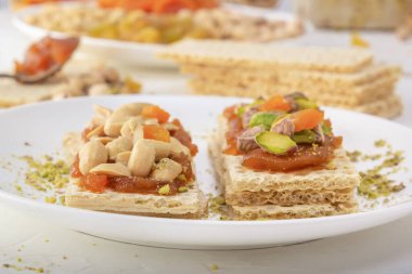 Fıstıklı, fıstıklı, kuru üzümlü ve şekerli gevrek, düşük kalorili buğday krakerleri beyaz bir tabakta kayısı reçeli ve arka planda oryantal tatlılar. Yakın plan.