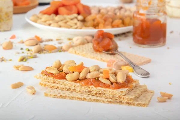 Düşük kalorili gevrek buğday krakerleri, fıstık ve kuru kayısı ile beyaz bir masada kayısı reçeli tabakası ve doğu tatlılarının arka planında. Yakın plan.