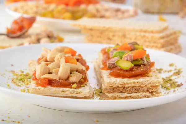 Fıstıklı, fıstıklı, kuru üzümlü ve şekerli gevrek, düşük kalorili buğday krakerleri beyaz bir tabakta kayısı reçeli ve arka planda oryantal tatlılar. Yakın plan.