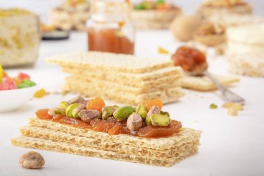 Crispy low-calorie wheat crackers with pistachios and candied fruits on a thin layer of apricot jam on a white table against a background of oriental sweets. Close-up