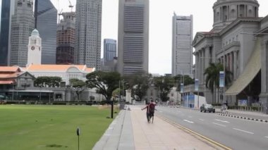 Singapur, Singapur - 08 Ocak 2020. Bir kadın ve bir erkek, şehrin merkezinde ıssız bir kaldırım boyunca gökdelenlerin ve kriket kulübünün arka planına karşı birlikte yürüyorlar.