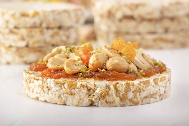 Beyaz ahşap bir masada kayısı reçeli ince bir tabaka üzerinde fıstık ve kurutulmuş kayısı ile patlamış buğday taneleri. Yakın plan.