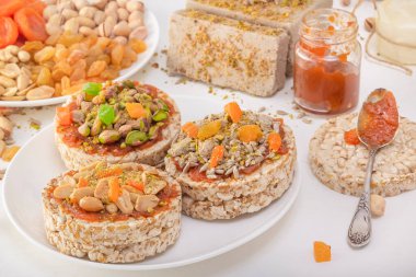 Fıstıklı patlamış buğday taneleri ve kurutulmuş kayısılar, şam fıstıkları ve ayçekirdeği, halva ve kuru üzümler beyaz bir tabakta kayısı reçeli ve doğu tatlılarının arka planında.