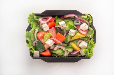 Taze salatalık, domates, dolmalık biber, marul, kırmızı soğan, beyaz arka planda tek kullanımlık kağıt kutuda zeytinyağlı beyaz zeytin yağı ve feta peyniri. Yemek teslimatı konsepti. Üst görünüm