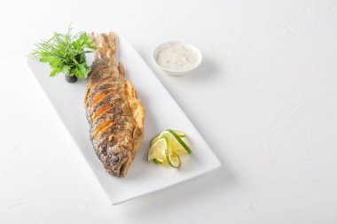 Arka planda beyaz bir tabakta otlu, soslu ve limonlu kızarmış alabalık. Boşluğu kopyala