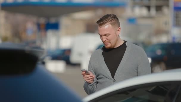 Der junge Mann kostet auf dem Parkplatz und druckt SMS — Stockvideo