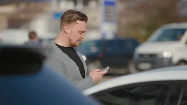 O jovem custa no estacionamento e algo olha no telefone . — Vídeo de Stock