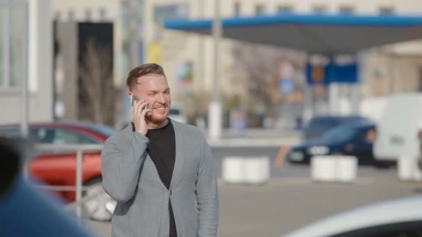 Der junge Mann geht auf den Parkplatz und telefoniert — Stockvideo