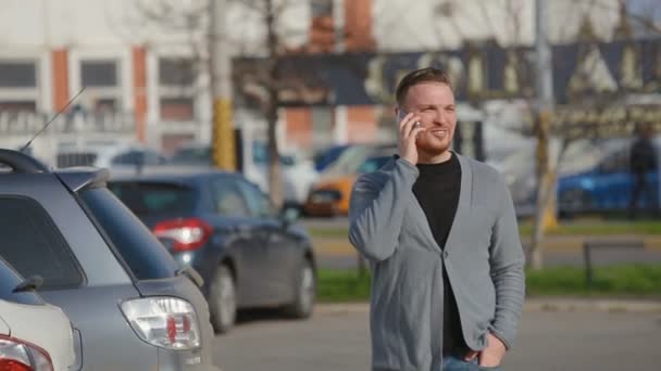 Den unge mannen går på parkering och talar via telefon — Stockvideo