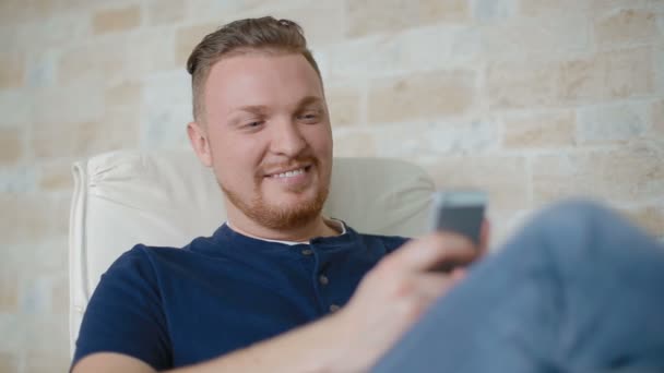 Молодий чоловік посміхається і листується з кимось по телефону — стокове відео