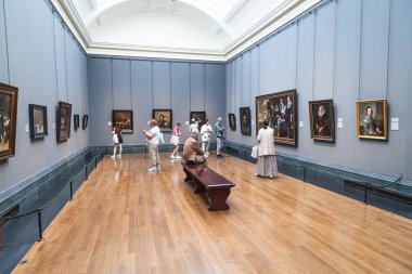 Londra 'daki Ulusal Galeri' nin içinde. Ziyaretçiler, sakin, ahşap zemin, bir bank ve yüksek kemerli tavan pencereli, ışık dolu bir salondaki çerçeveli başyapıtlara hayran. Londra, İngiltere, 28 Haziran 2023