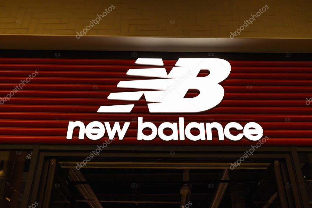 Illuminated New Balance logo sign on a retail storefront facade, showcasing the athletic footwear brands identity in an urban shopping setting. London, UK, 29 June 2023