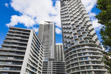 Mavi gökyüzünün altında kavisli balkonları ve cam cepheleri olan modern konut kulelerinin yukarıdan görünüşü.