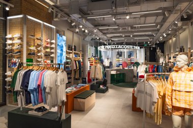 Çağdaş giyim mağazası sahnesi bir Lacoste dükkanında, sıcak ışıklandırma ve sergilenen sergilerle. Londra, İngiltere, 4 Temmuz 2023