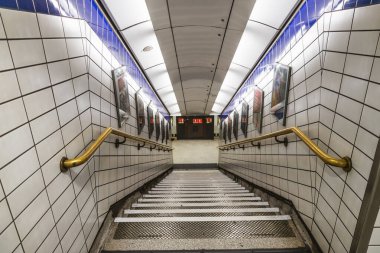 Beyaz fayanslı, mavi aksanlı ve pirinç raylı Londra metro merdiven boşluğunun simetrik görüntüsü. Londra, İngiltere, 4 Temmuz 2023