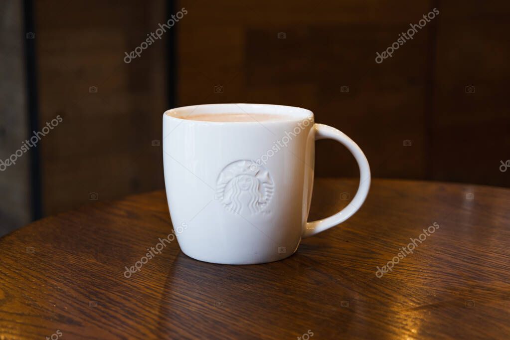 Minimal cafe scene with a clean white Starbucks mug on polished wood, blurred background and warm tones. London, UK, 8 July 2023