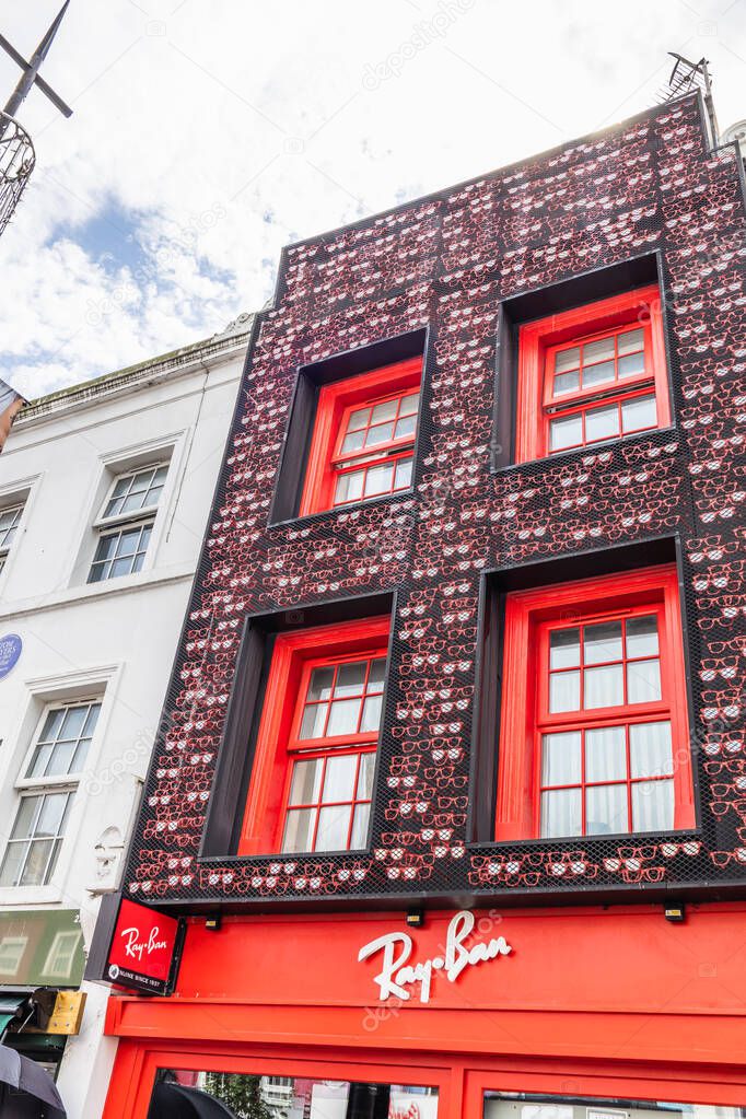 Vibrant Ray Ban storefront with red facade and patterned brickwork, showcasing brand signage and urban retail architecture on a lively high street. London, UK, 8 July 2023