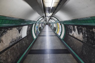 Boş Londra metro koridoru, hareketli yürüyüş yolu, kaybolan nokta simetrisi, şehir içi geçiş mimarisi ve kumlu dokuları gösteriyor. Londra, İngiltere, 9 Temmuz 2023