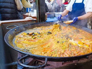 Geleneksel İspanyol paella 'sı dev bir tavada cızırdıyor ve bir satıcı hareketli bir sokak yiyecek pazarını karıştırıyor. Londra, İngiltere, 17 Aralık 2023
