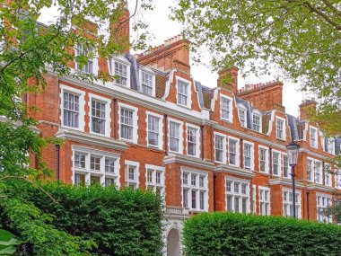 Londra 'da, yapraklı ağaçlar ve çitlerle çerçevelenmiş beyaz kuşak pencereleri, gablonları ve bacaları olan klasik kırmızı tuğlalı evler..