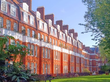 Klasik Londra kırmızı tuğlalı evler, yüksek bacaları, yemyeşil ve parlak mavi gökyüzü. Tarihi mimari ve barışçıl yerleşim ortamı.
