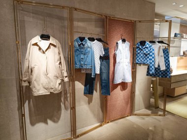 Lüks Louis Vuitton mağazasının iç mimarisi ahşap raflarda, kot setlerinde, ceketlerde ve elbiselerde minimalist, lüks bir butik ortamda tasarımcı kıyafetleri sergiliyor. Londra, İngiltere, 8 Haziran 2024