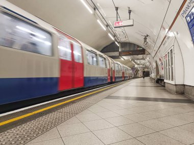Boş bir platformun yanından geçen Londra metrosunun dinamik görüntüsü, hız, kentsel ulaşım ve şehir altyapısını vurguluyor..