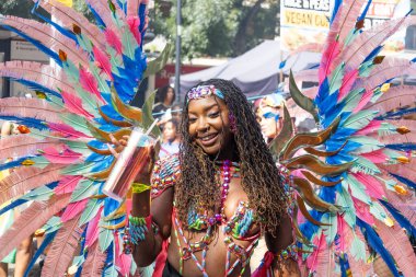 Notting Hill 2023 'te parlak tüylü kostümlü, gülümseyen bir karnaval dansçısı. Parlak renkler, geçit töreni enerjisi, Karayipler festivali havası. Londra, İngiltere, 28 Ağustos 2023