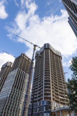 Modern bir gökdelenin yanındaki yüksek açılı bir kule vincin dramatik alçak açılı görüntüsü, bulutlu açık mavi gökyüzü altında kentsel gelişim ve mimariyi gösteriyor. Londra, İngiltere, 23 Eylül 2023