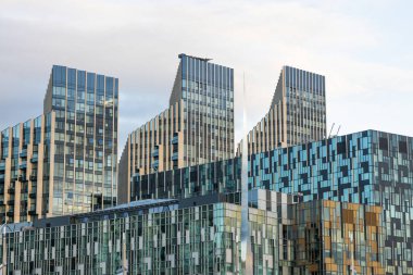 Benzersiz cam cepheli ve geometrik desenli çoklu modern binaların bulunduğu çağdaş kentsel mimarinin büyüleyici görüntüsü.