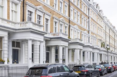Klasik Londra teraslı evlerin, zarif Viktorya dönemi mimarisinin sergilendiği resimli bir sıra. Arabalar sakin yerleşim caddesi boyunca park halinde. Londra, İngiltere, 28 Ekim 2023