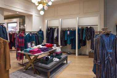 Modern bir giyim mağazasının parlak ve davetkar iç mimarisi şık kadın kıyafetleri ve sergi masalarıyla dolu. Londra, İngiltere, 28 Ekim 2023