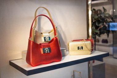 İki şık kadın çantası, biri canlı kırmızı, biri zarif bej, modern moda mağazasında temiz beyaz bir rafta sergileniyor. Londra, İngiltere, 28 Ekim 2023