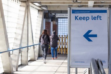 Mavi oklu beyaz bir tabela, yayalara şehir ortamında geçici olarak kapalı bir geçitte yürürken sola dönmelerini emreder..