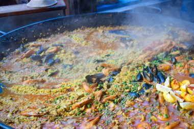 Geleneksel İspanyol deniz ürünleri paella 'sının sokak pazarında büyük bir tavada pişirilmesi. Midye, karides ve safran çorbası ile sıcak pilav tabağı..