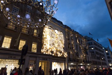 Lüks mağazaların ön planlarının ve Londra 'nın kalabalık bir caddesini gece aydınlatacak şenlikli dekorasyonların odağından çıkarılmış bokeh arka planı. Londra, İngiltere, 17 Aralık 2023