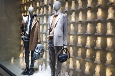 Lüks bir butik vitrin vitrininde dekoratif ışıklandırılmış arka planda modern ceket ve aksesuarlar sergileyen iki şık manken. Londra, İngiltere, 17 Aralık 2023