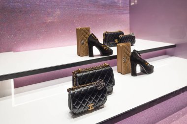 Siyah örtülü çantalar, yüksek topuklu ayakkabılar ve mor arka planda beyaz raflarda markalı aksesuarlar bulunan lüks bir Chanel mağazası vitrini. Londra, İngiltere, 17 Aralık 2023