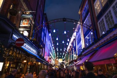Londra 'daki Carnaby Caddesi' nin gece görüş alanının dışında. Soho bölgesinde kalabalık bir kalabalıkta asılı duran soyut mavi ve mor renkli ışıklar. Londra, İngiltere, 17 Aralık 2023