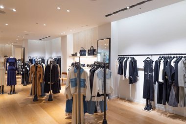 Modern bir giyim mağazasının iç kısmının soyut arka planı. Giysi rafları, ahşap döşemeler ve parlak ışıklandırmayla bir moda butiğinin odaksız görüntüsü. Londra, İngiltere, 24 Aralık 2023